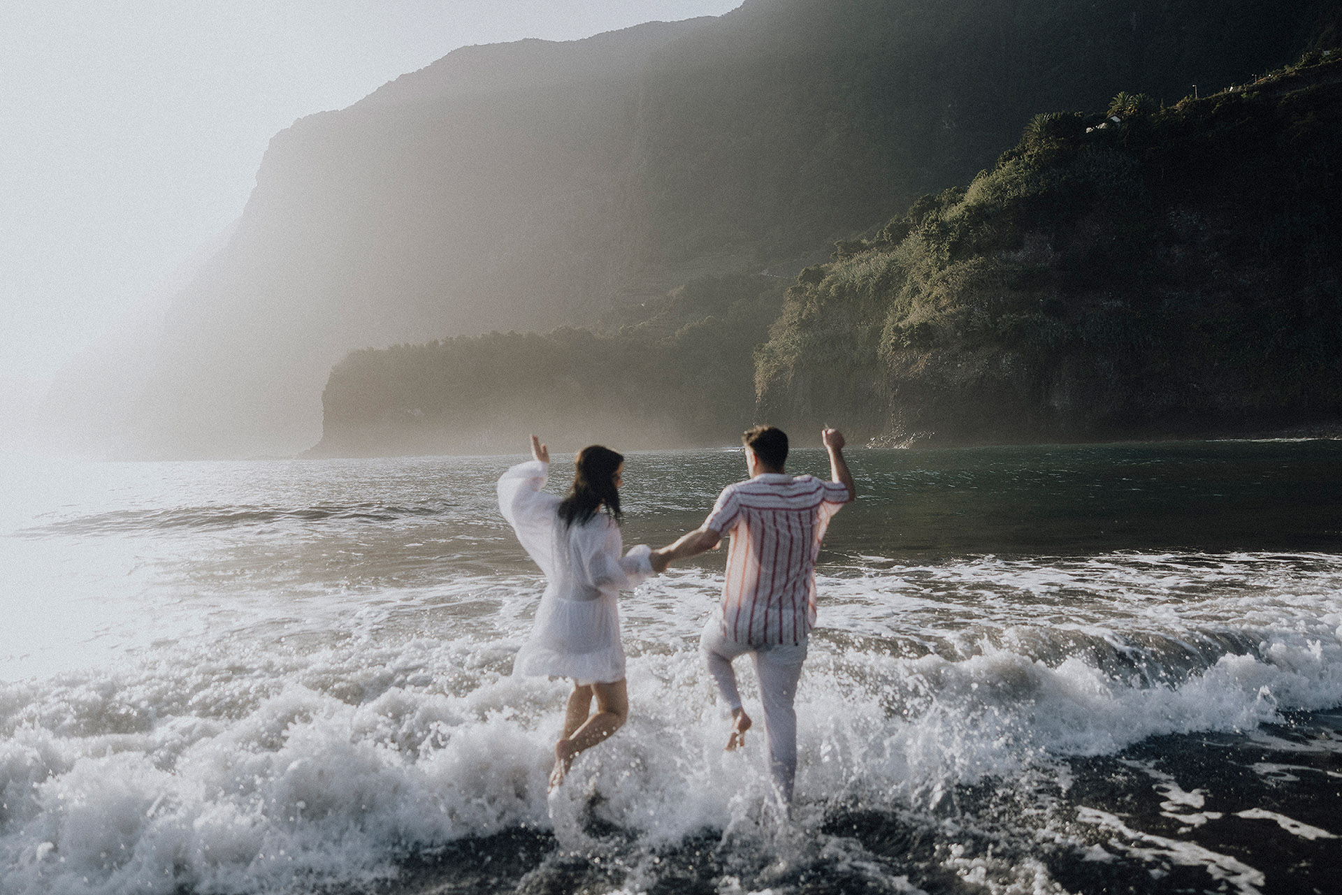 Sesja na Maderze. Para młoda biegnąca w falach oceanu na tle gór, sesja poślubna o wschodzie słońca na plaży Seixal, Madera. Zdjęcie: Camera Folks Wedding Photo & Video