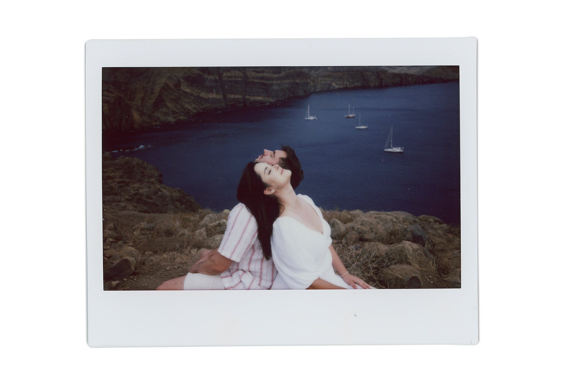 Skan zdjęcia Polaroid przedstawiający parę młodą siedzącą tyłem do siebie na klifie, patrzącą w niebo, w tle zatoka z jachtami, Ponta de São Lourenço, Madera, analogowa fotografia ślubna.