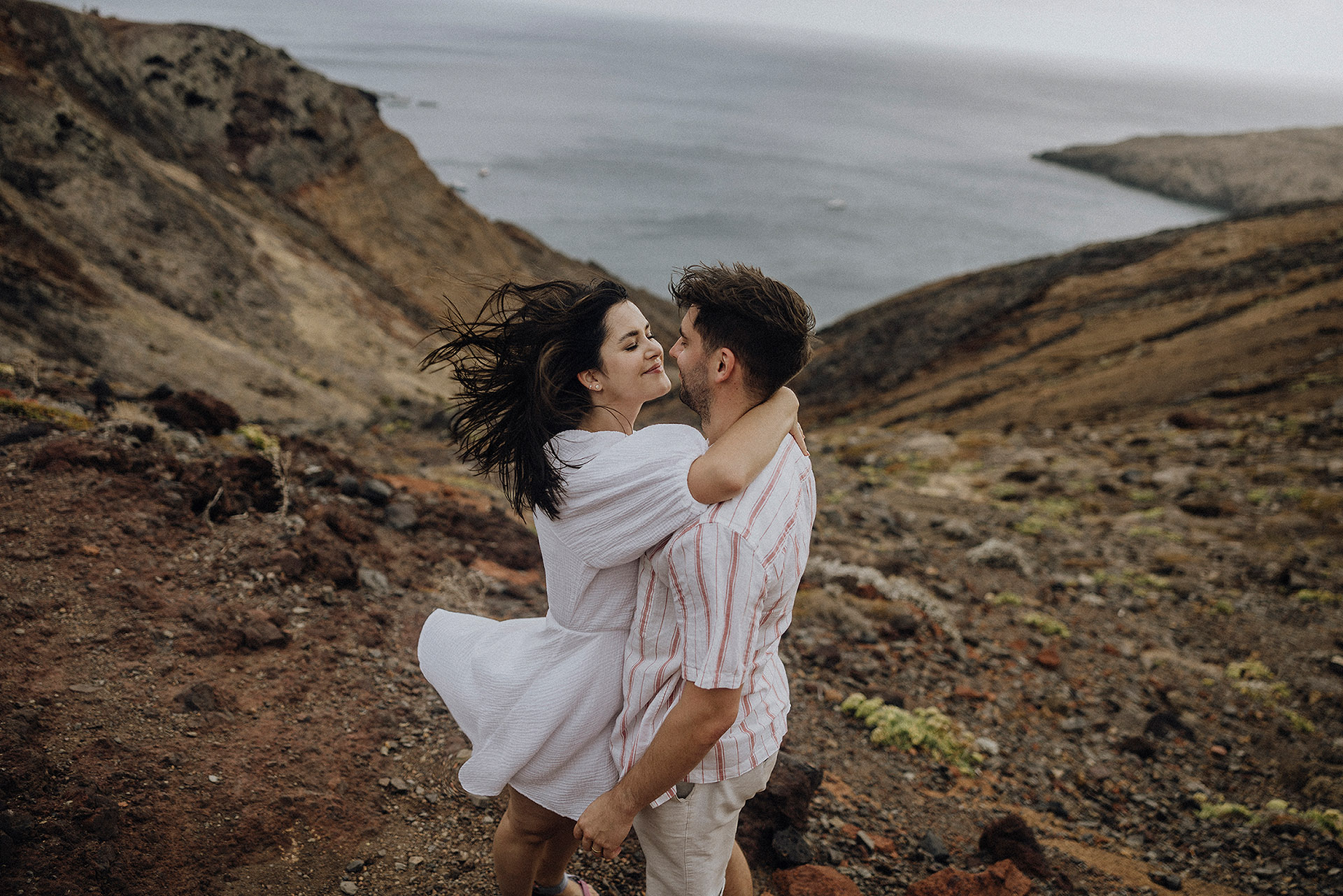 Sesja na Maderze. Para młoda w objęciach na skalistym wzgórzu Ponta de São Lourenço na Maderze, wiatr rozwiewa włosy, sesja poślubna by Camera Folks Wedding Photo & Video.