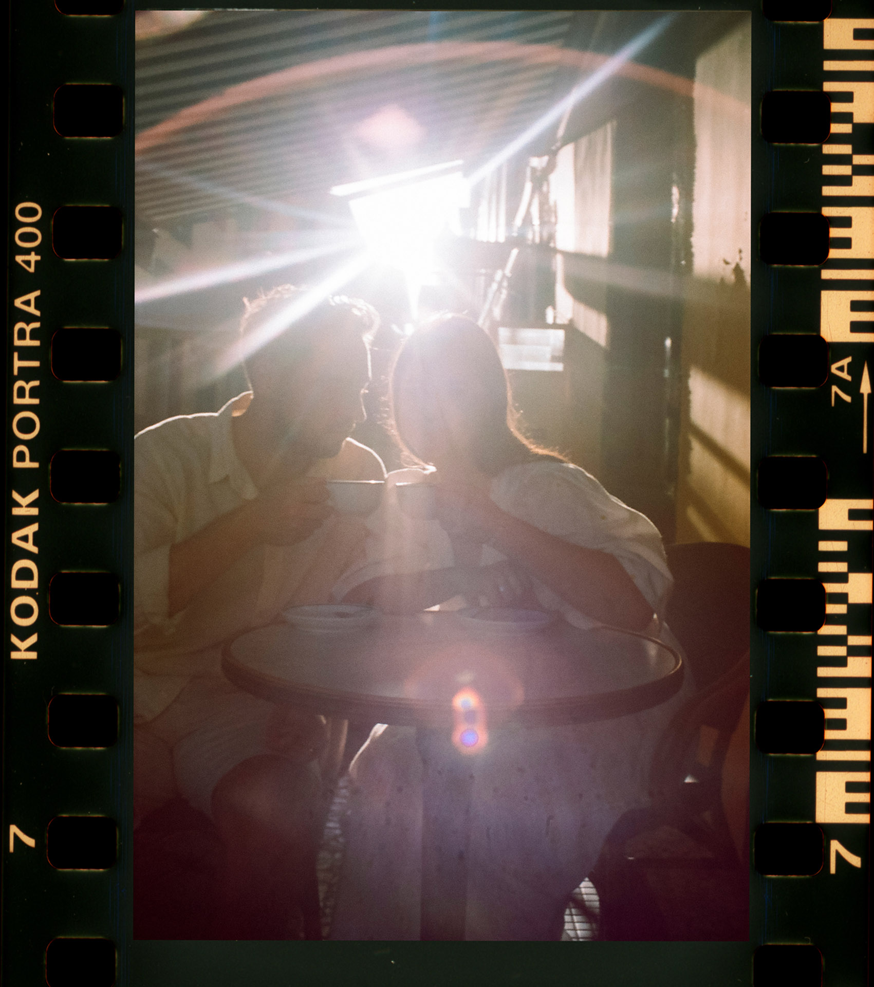Skan analogowy K&D w kawiarni w Funchal na Maderze, intymny moment przy stoliku z efektem flary świetlnej, fotografia ślubna analogowa by Camera Folks Wedding Photo & Video.