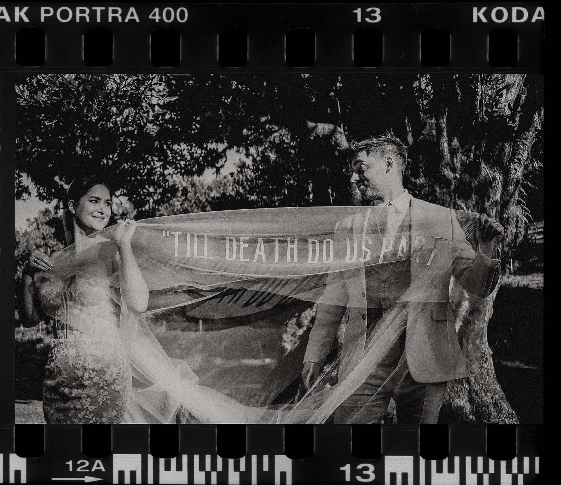 Czarno-biały skan z kliszy przedstawiający parę K&D trzymającą welon z napisem "TILL DEATH DO US PART", inspirowany welonem Hailey i Justina Bieber, sesja plenerowa od Camera Folks - Wedding Photo & Video
