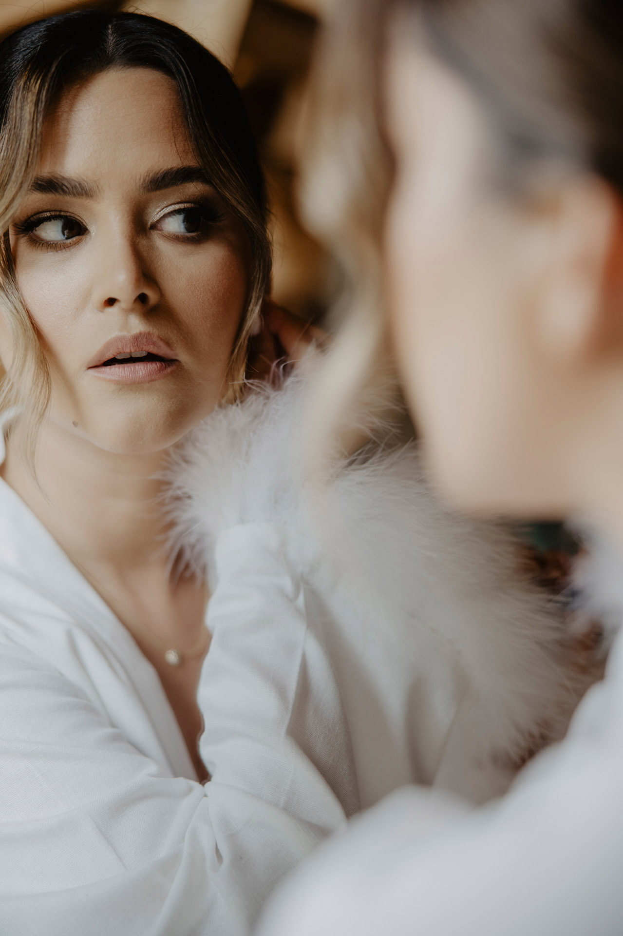 Panna Młoda w białym peniuarze, patrząca w lustro podczas przygotowań do ślubu w domku w Sielsko Anielsko, sfotografowana przez Camera Folks – Wedding Photo & Video.