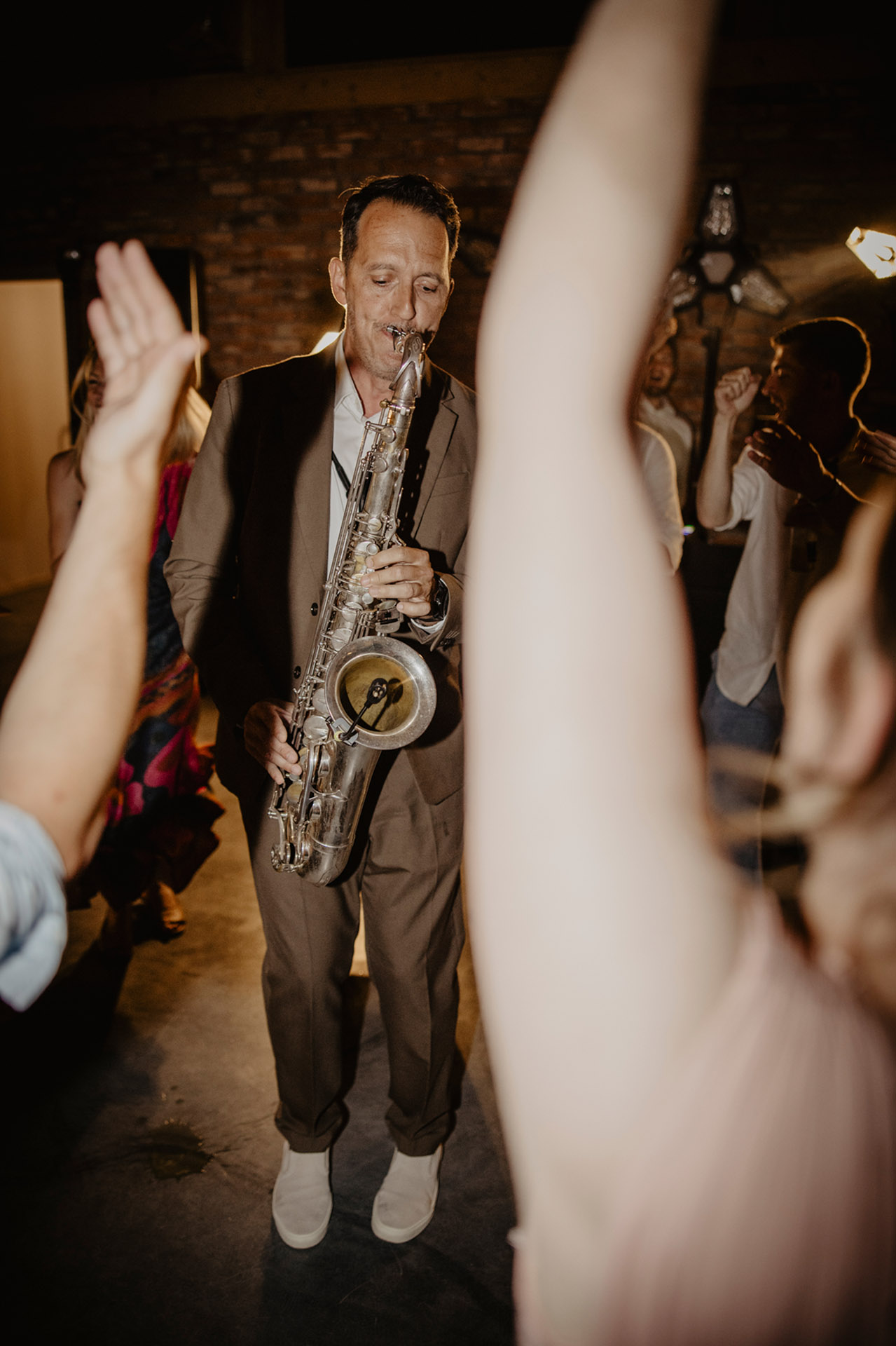 Saksofonista w brązowym garniturze grający na saksofonie altowym, otoczony roztańczonymi gośćmi na parkiecie, podczas wesela w Sielsko Anielsko, wykonawca: Wedd & Sax (@weddandsax), sfotografowany przez Camera Folks – Wedding Photo & Video.